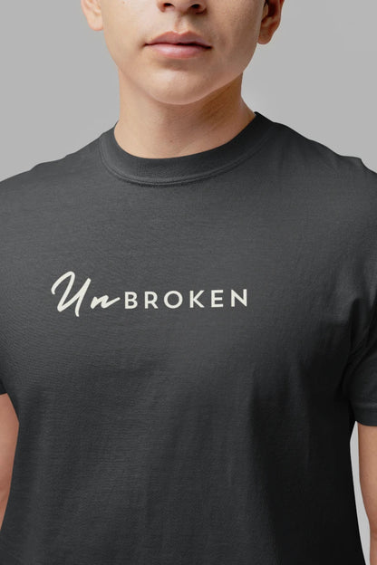 A close-up of a person wearing a dark steel grey t-shirt with the text 'Un-BROKEN' printed in white across the chest.
