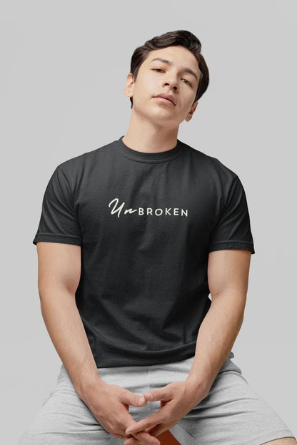 A man wearing a steel grey crewneck t-shirt with the white text 'UnbROKEN' printed across the chest, paired with light gray shorts, set against a solid gray background.