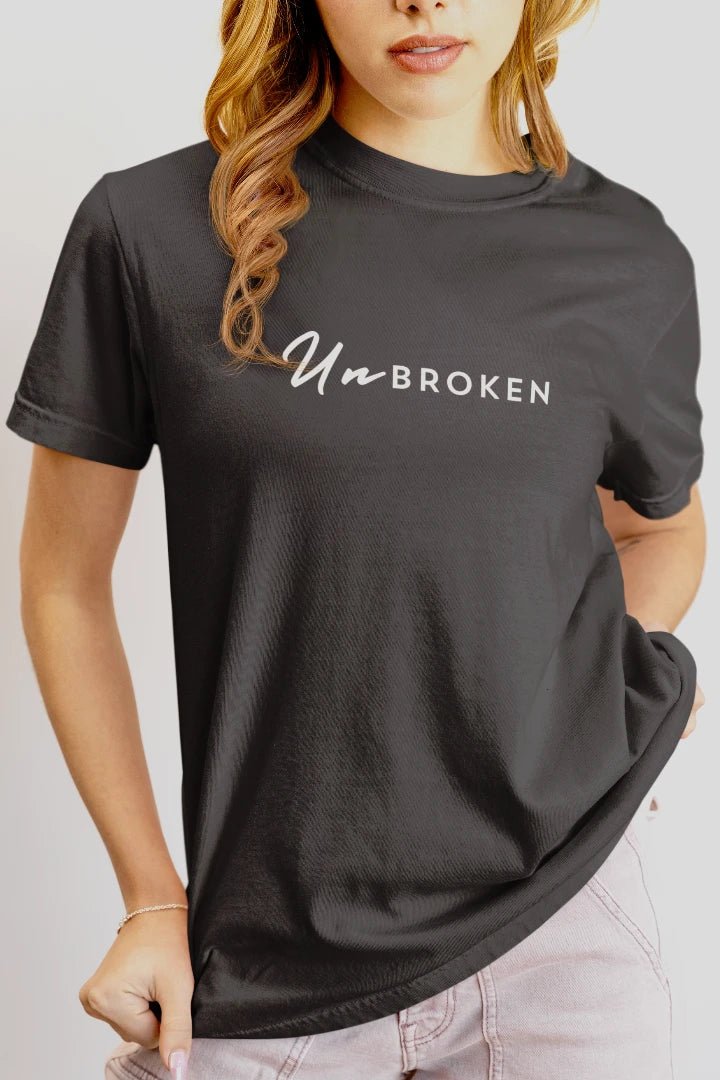 A woman wearing a steel grey short-sleeve t-shirt with the words 'UnBROKEN' printed across the chest in white. The photo is cropped from the mouth down to the hips, showing the fit of the shirt against a light gray background.