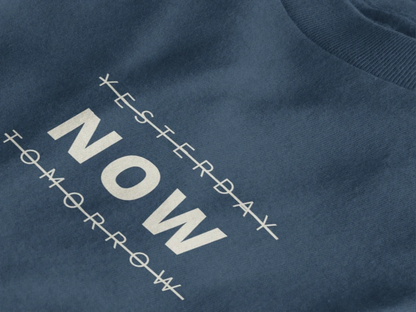 Close-up of a midnight navy crewneck t-shirt featuring a black graphic print that reads 'NOW' crossed out with lines above and below it, with 'YESTERDAY' and 'TOMORROW' 