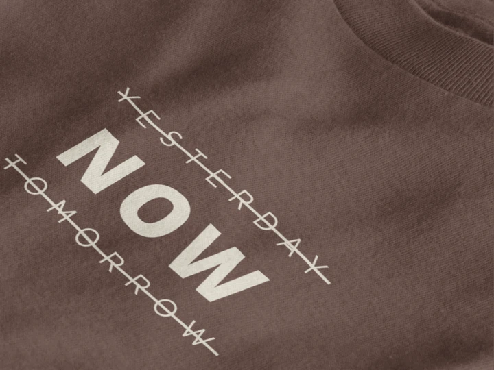 Close-up of a dark mocha crewneck t-shirt featuring a black graphic print that reads 'NOW' crossed out with lines above and below it, with 'YESTERDAY' and 'TOMORROW' 